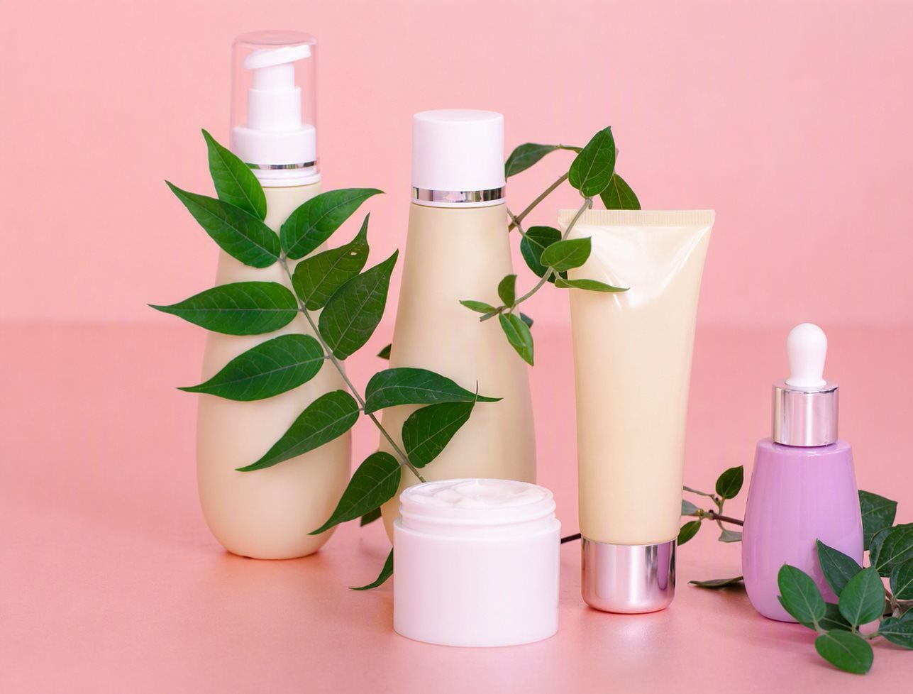 Set de skincare de cinco piezas con hojas verdes sobre fondo rosa